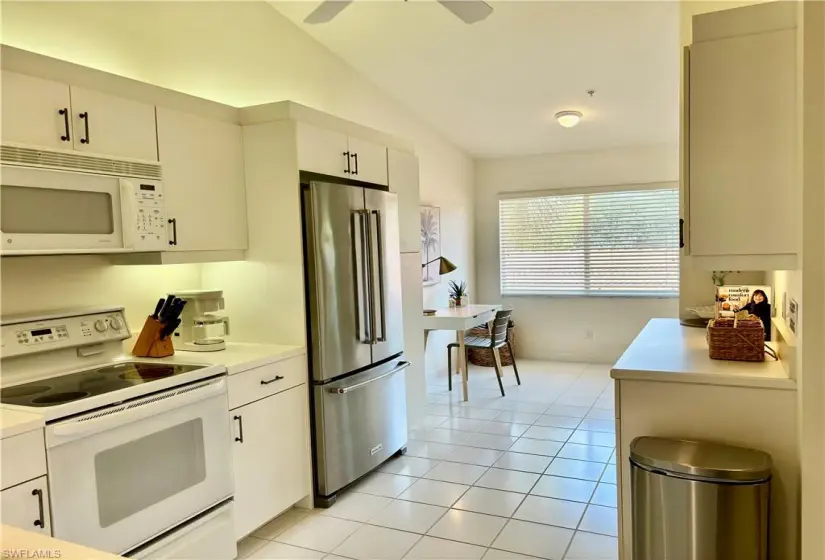 Kitchen with ceiling fan, light tile floors, white appliances, and lofted ceiling