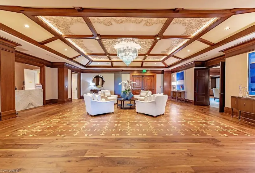 Unfurnished living room with beam ceiling, wood-type flooring, an inviting chandelier, coffered ceiling, and ornamental molding