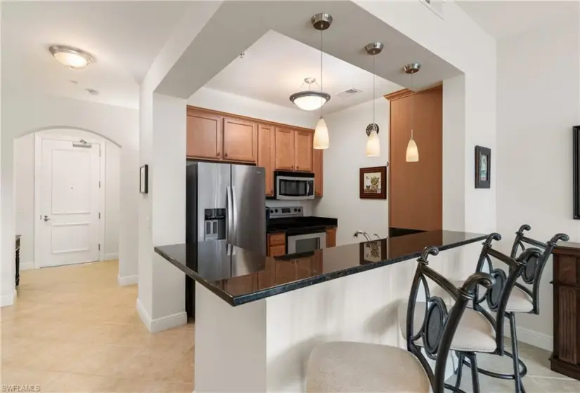 Kitchen with stainless steel appliances, a kitchen breakfast bar, hanging light fixtures, dark stone countertops, and light tile floors