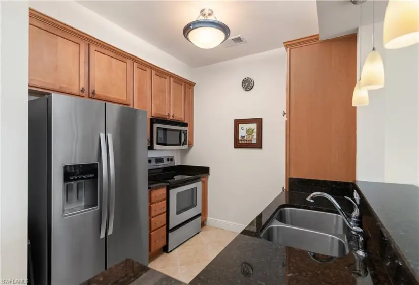 Kitchen with dark stone counters, stainless steel appliances, light tile flooring, pendant lighting, and sink