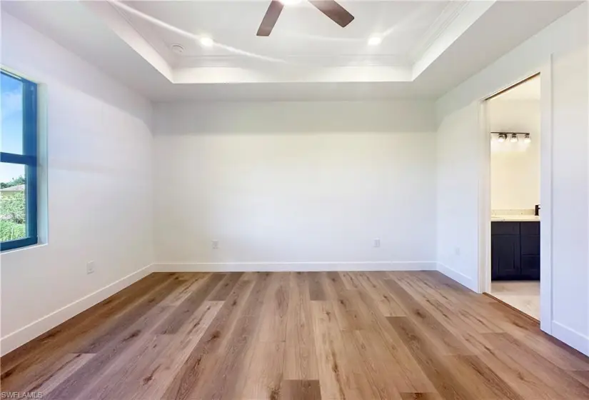 Unfurnished bedroom with ensuite bathroom, hardwood / wood-style floors, ceiling fan, and a raised ceiling