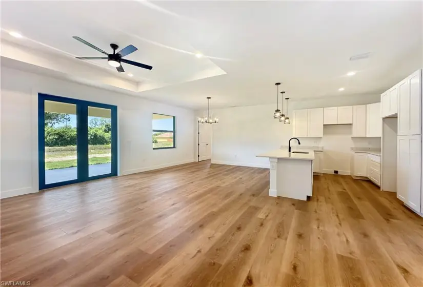 Kitchen featuring light wood-type flooring, ceiling fan with notable chandelier, sink, a kitchen island with sink, and white cabinetry