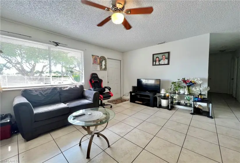 Living room with ceiling fan, a textured ceiling, and light tile floors