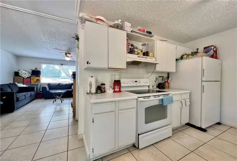 Kitchen with white cabinets, light tile flooring, a textured ceiling, and white appliances