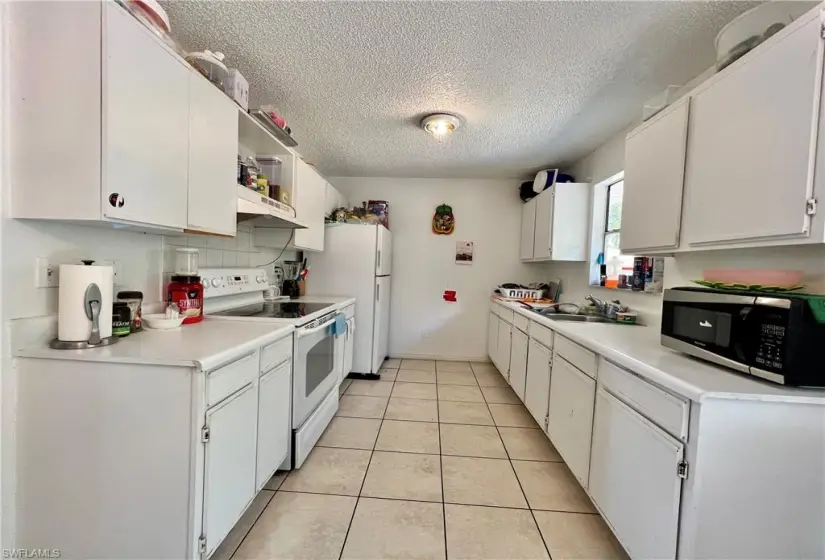 Kitchen with white cabinets, a textured ceiling, light tile floors, sink, and white range with electric cooktop